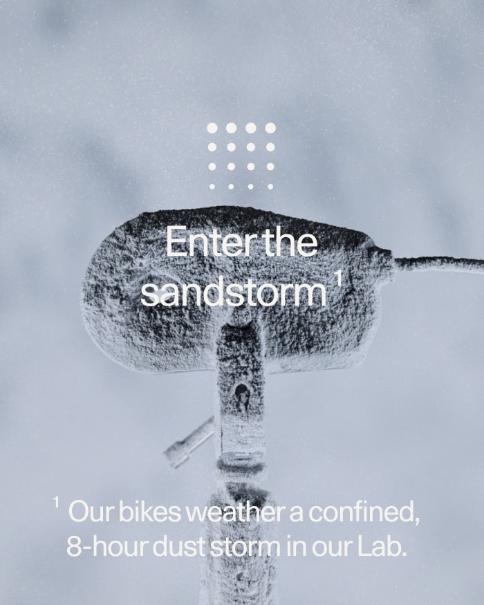 Vincent Venema | Sandstorm Bike Test Close-up of a bike handlebar covered in sand and dust, with text overlay about a sandstorm test in a lab environment.